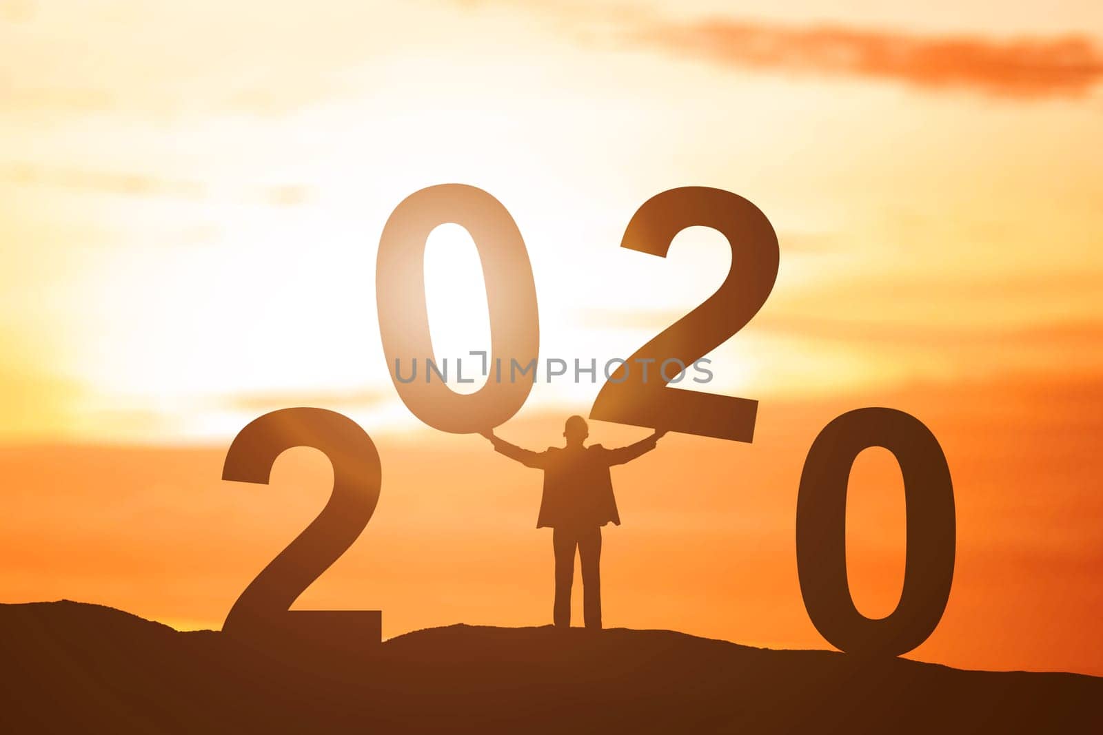 Silhouette of businessman put 2020 on the top of the hill with a sunset sky background. Happy New Year 2020