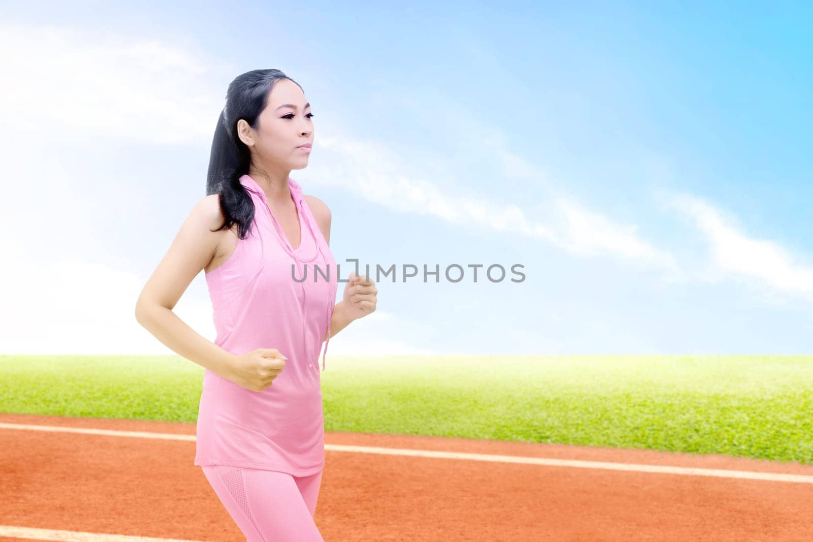 Asian runner woman running on the running track with a blue sky background