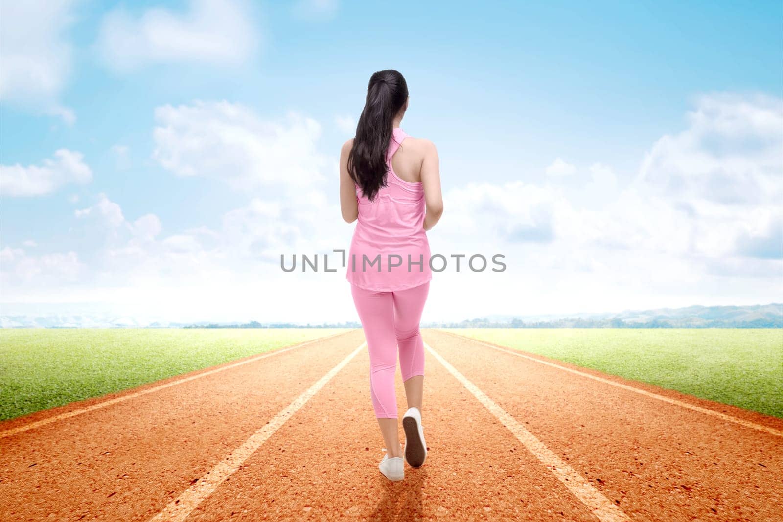 Rear view of Asian runner woman running on the running track with a blue sky background
