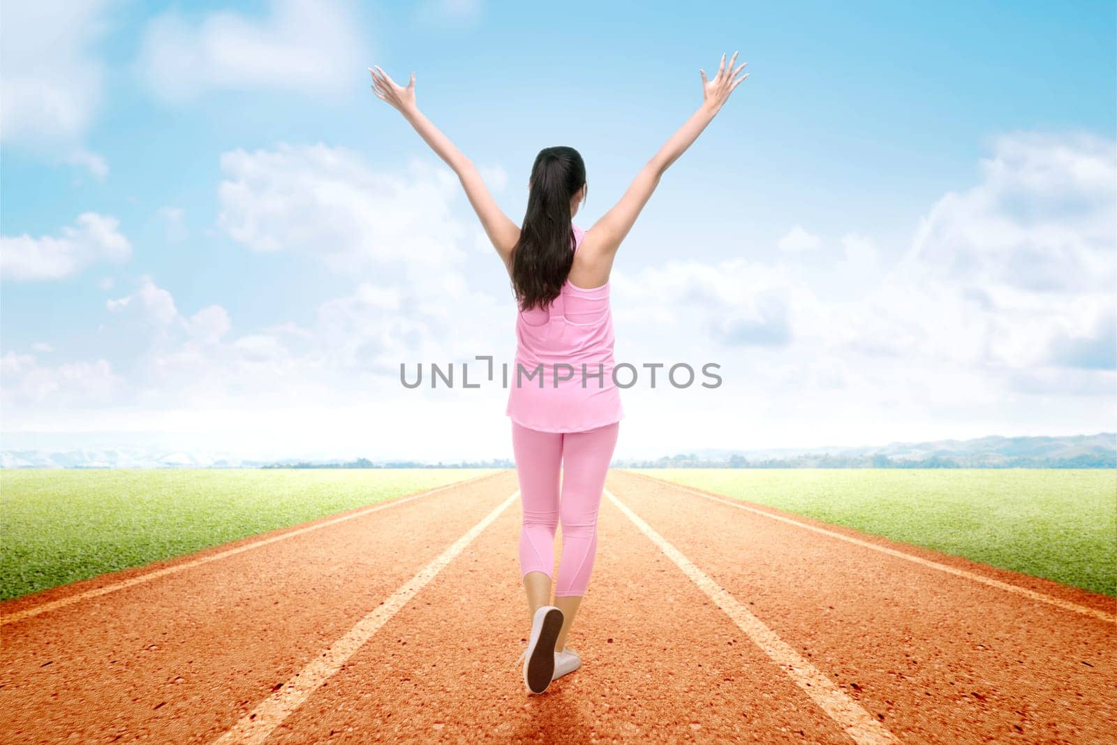 Rear view of Asian runner woman with excited expression after a run on the running track with a blue sky background
