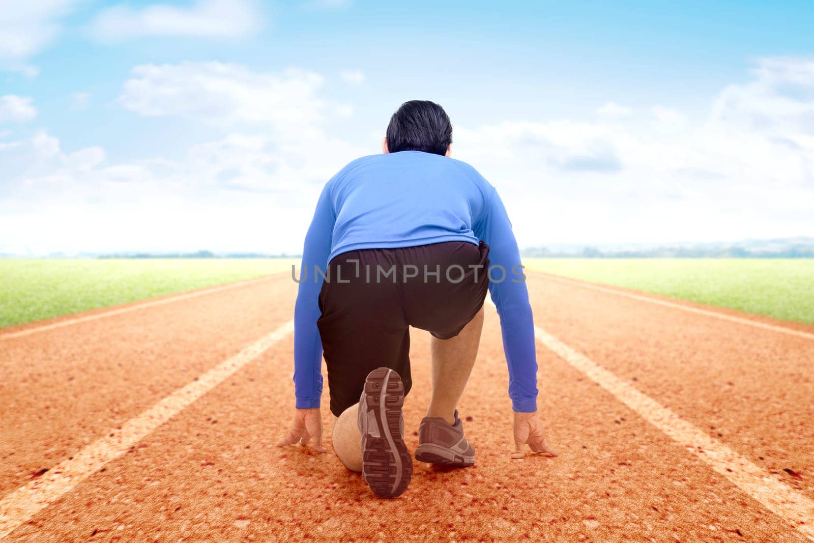 Rear view of Asian runner man ready to run on the running track with a blue sky background