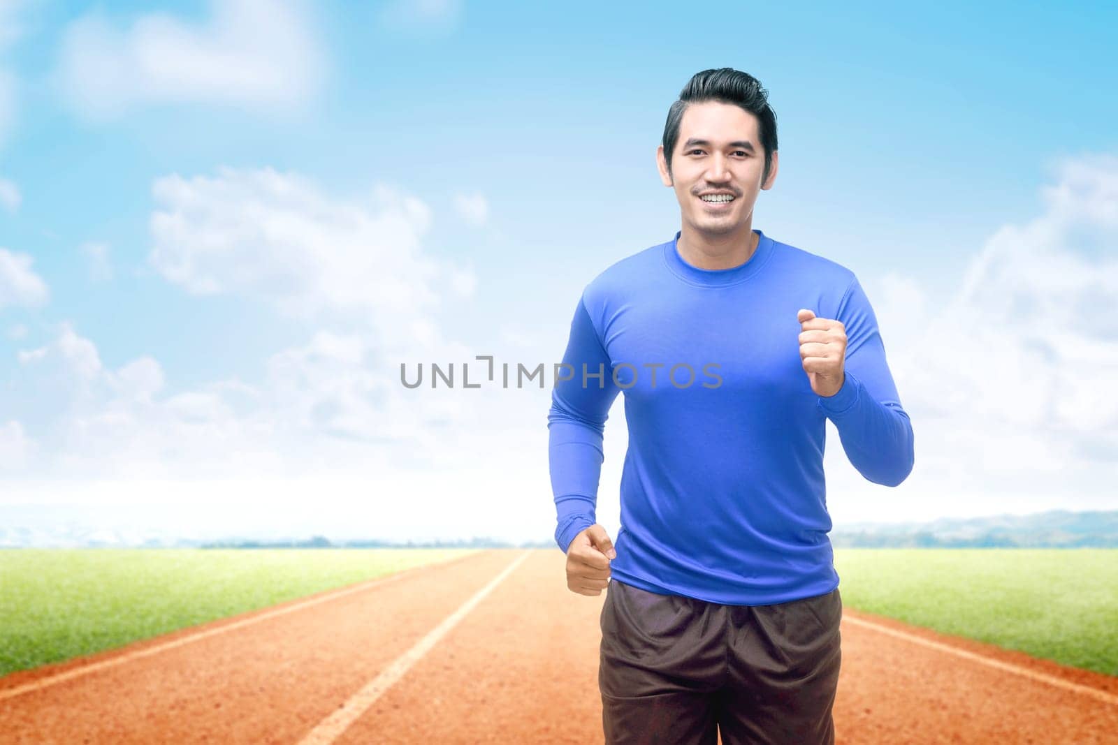 Asian runner man running on the running track with a blue sky background