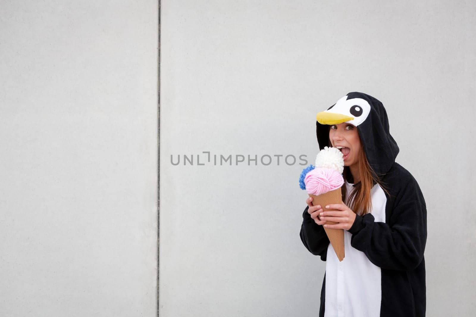 beautiful, young woman in penguin costume is eating decoration ice cream in front of concrete wall