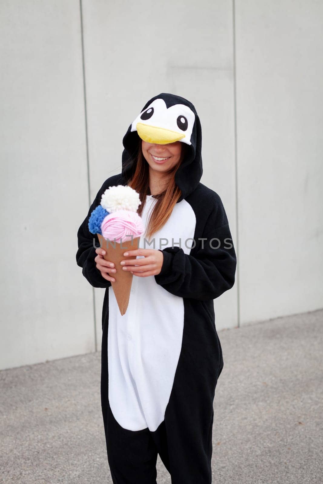 beautiful, young woman in penguin costume is eating decoration ice cream in front of concrete wall
