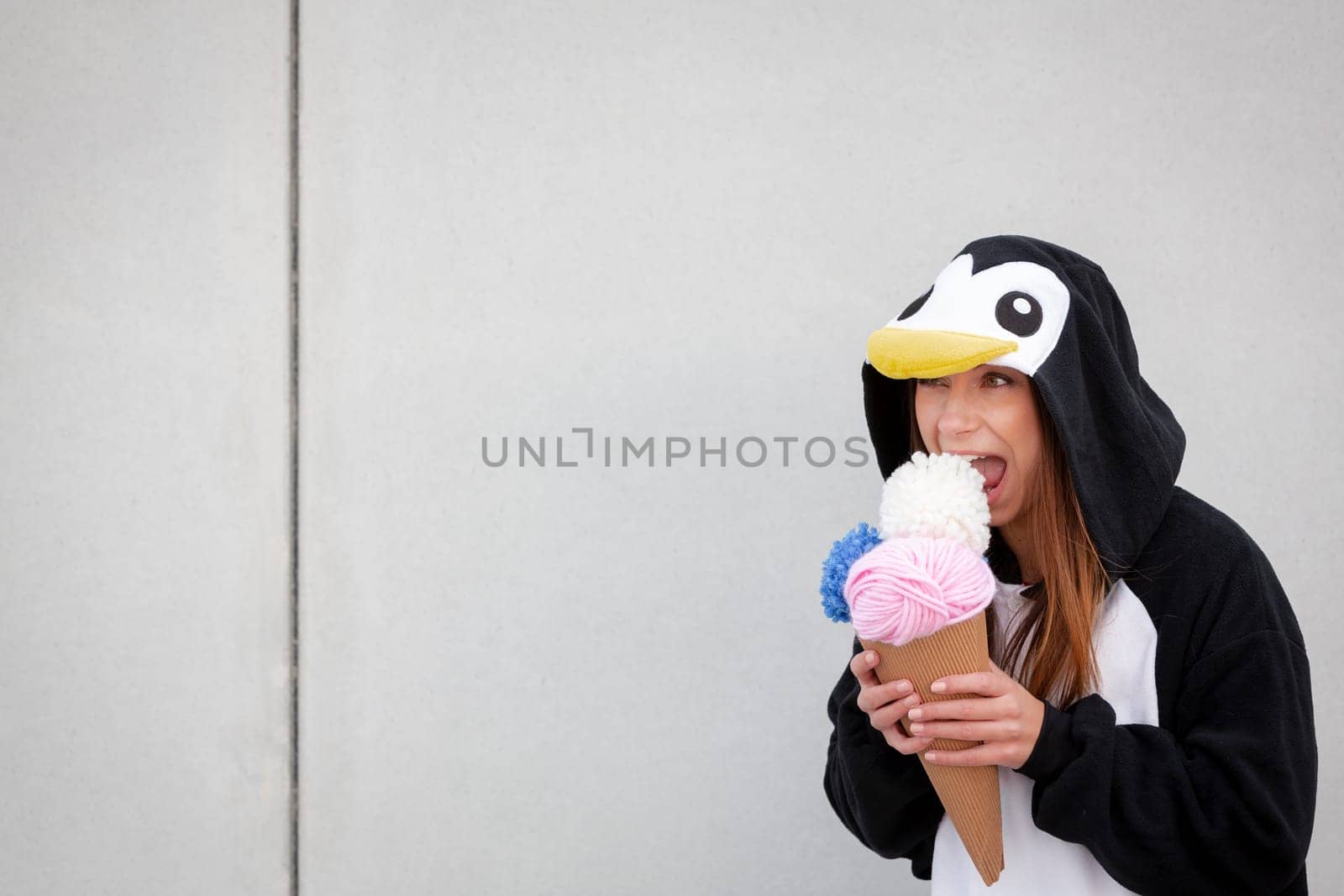 beautiful, young woman in penguin costume is eating decoration ice cream in front of concrete wall