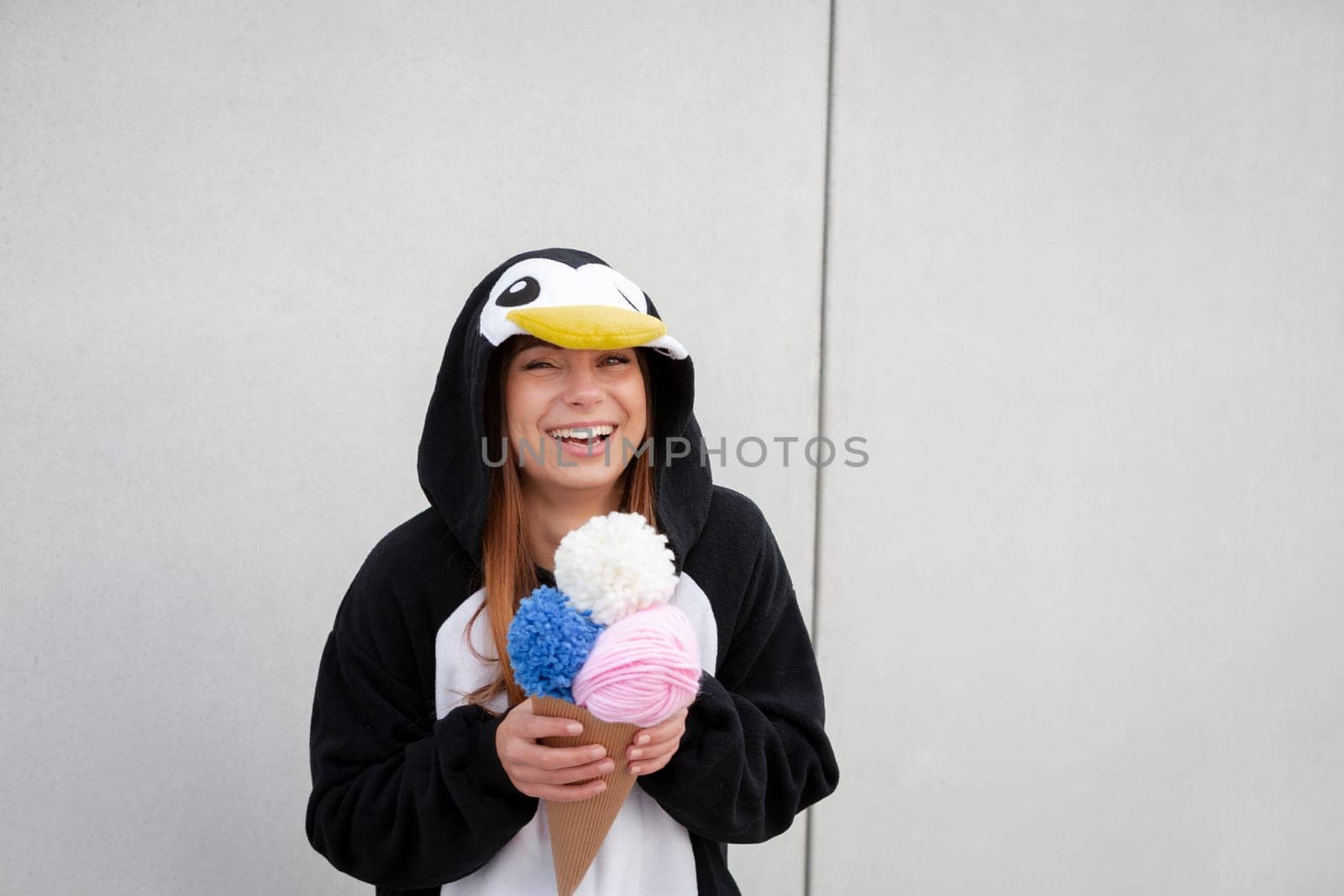 beautiful, young woman in penguin costume is eating decoration ice cream in front of concrete wall