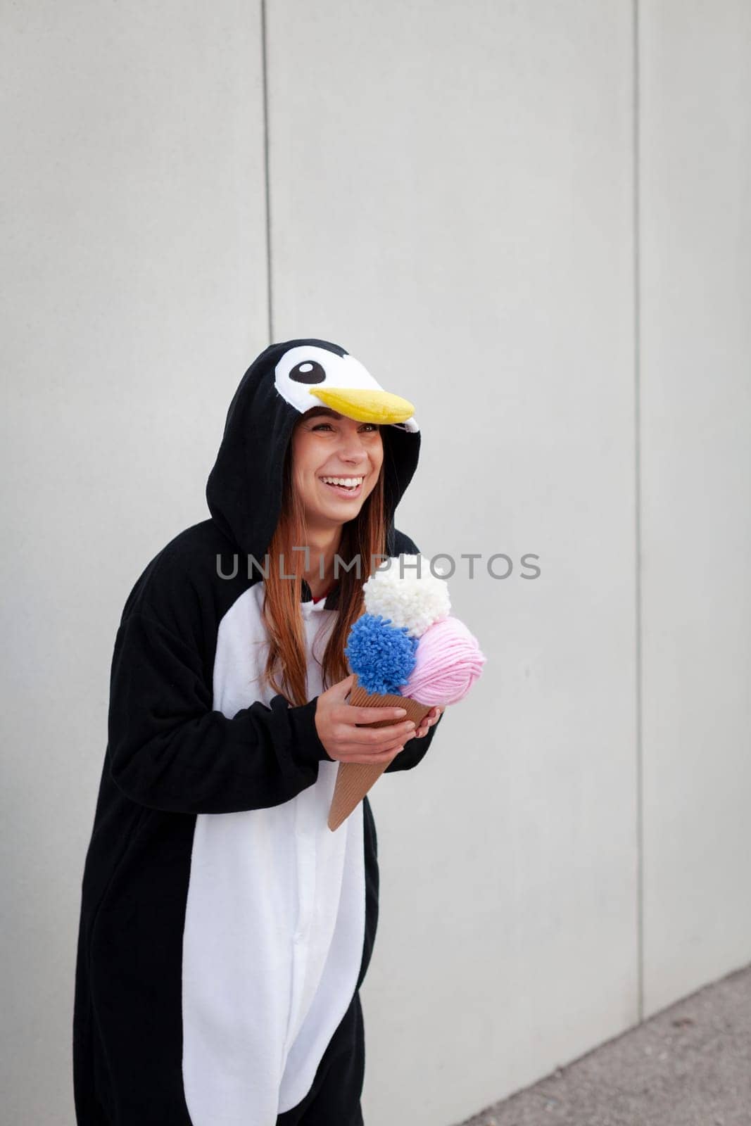 beautiful, young woman in penguin costume is eating decoration ice cream in front of concrete wall