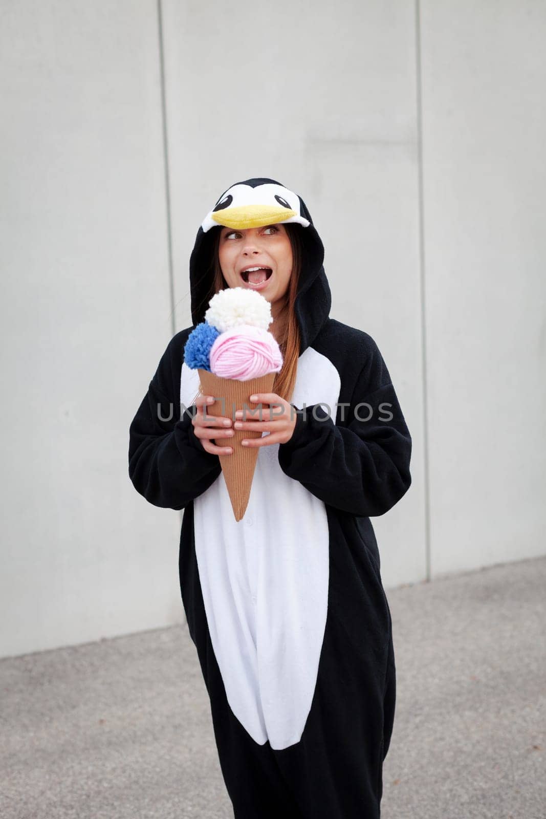 beautiful, young woman in penguin costume is eating decoration ice cream in front of concrete wall