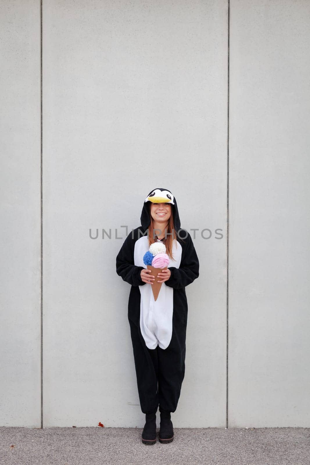 beautiful, young woman in penguin costume is eating decoration ice cream in front of concrete wall