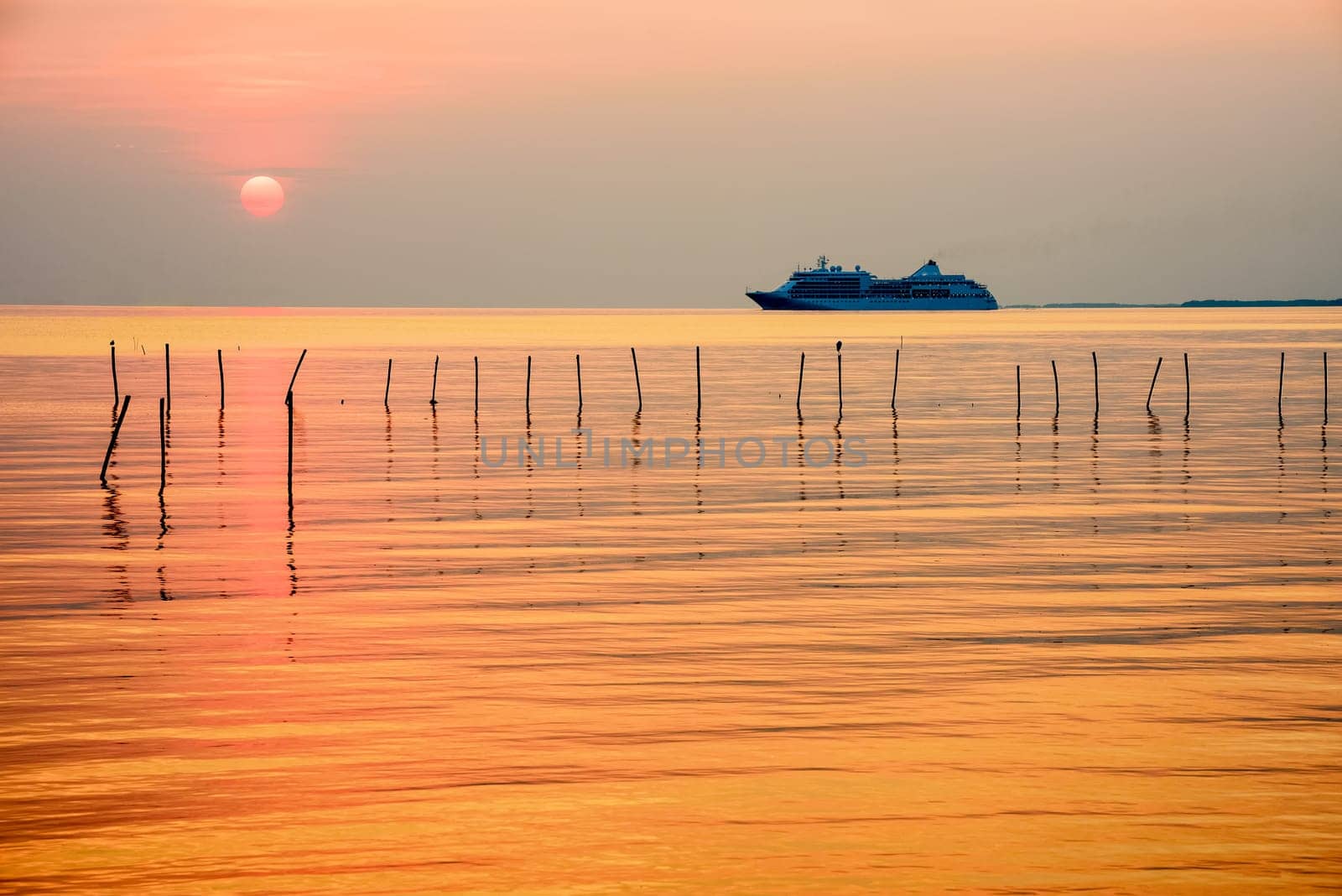 Travel by Cruise ship in the ocean, large luxury passenger boat is sailing on the bright sea, red sun in the colorful sky is yellow, orange, beautiful nature landscape at sunset or sunrise background