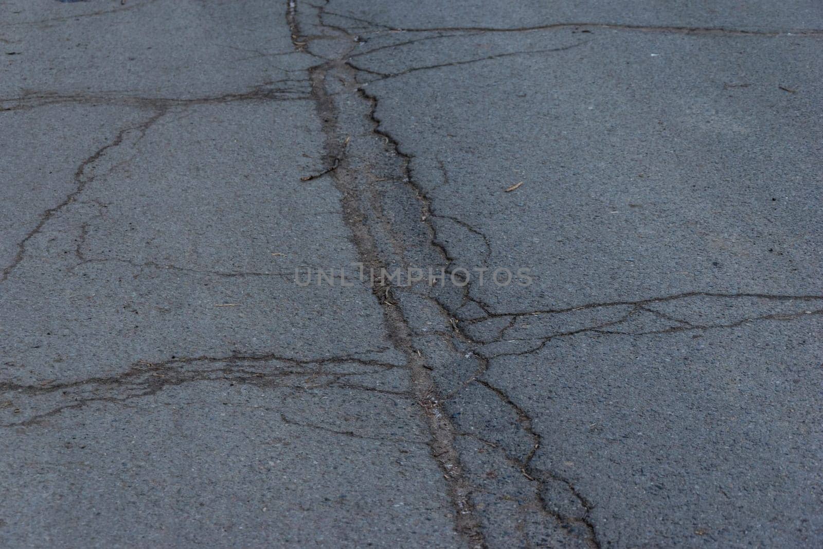 Asphalt road surface with small cracks and damages. Sidewalk asphalt road with cracks. Floor. Texture of tarmac road with cracks. Abstract background