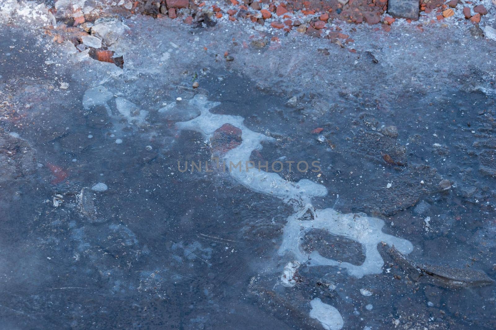 Frozen Puddle with broken ice. Ice Crust On Frozen Puddle. Winter background. Frozen puddle on the road. In January. Frozen Puddle And Dirt Road Close-Up.