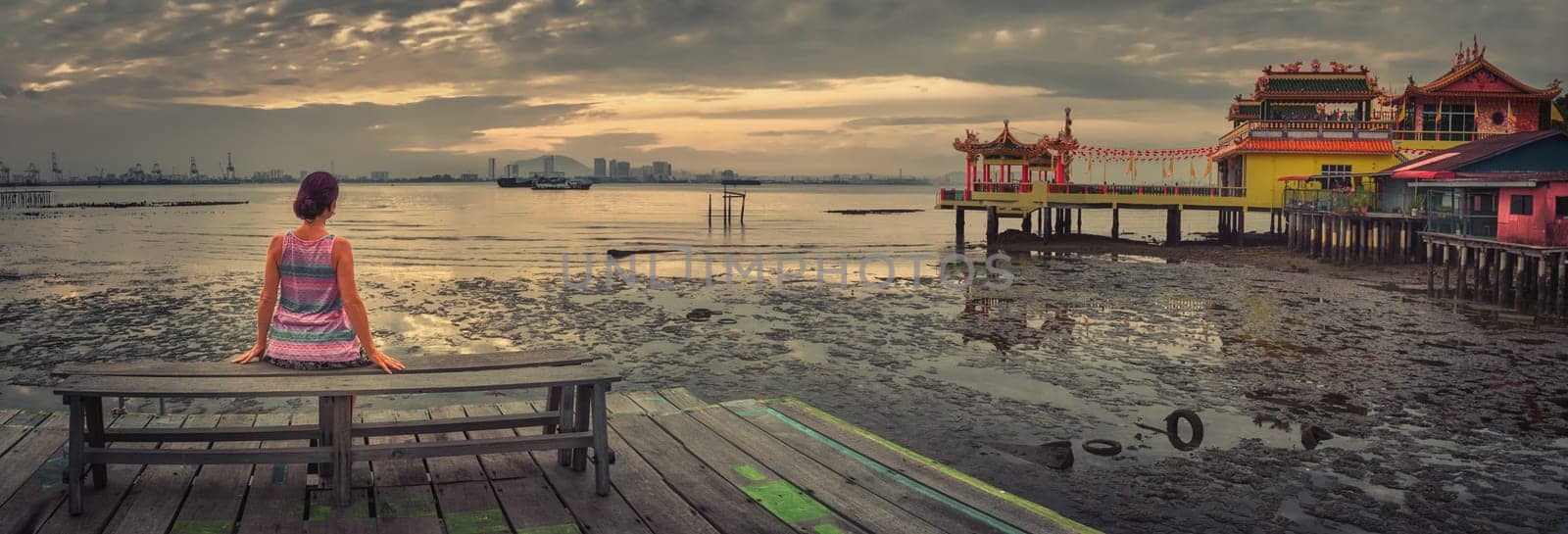 Tourist sitting at Yeoh jetty at sunrise, Georgetown, Penang, Malaysia. Panorama