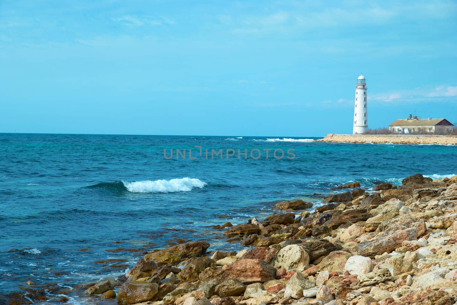 Old lighthouse on the sea coast. Storm, waves and blue sky.
