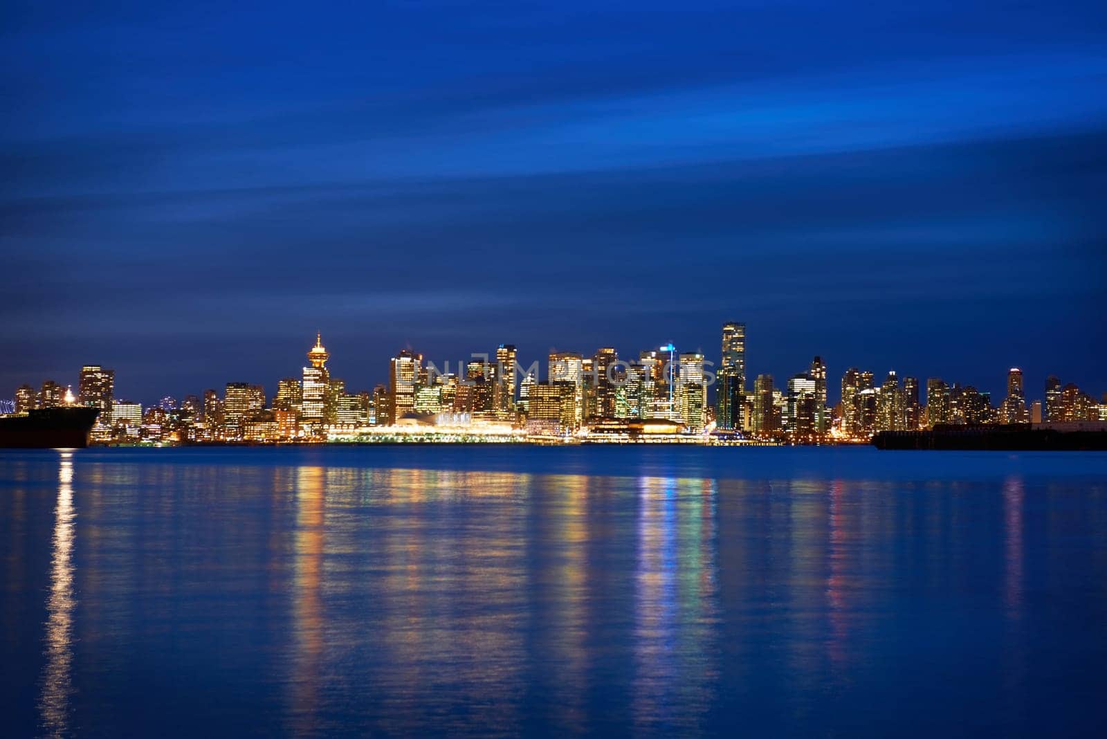 Night city, panoramic scene of downtown reflected in blue water. Vancouver, Canada
