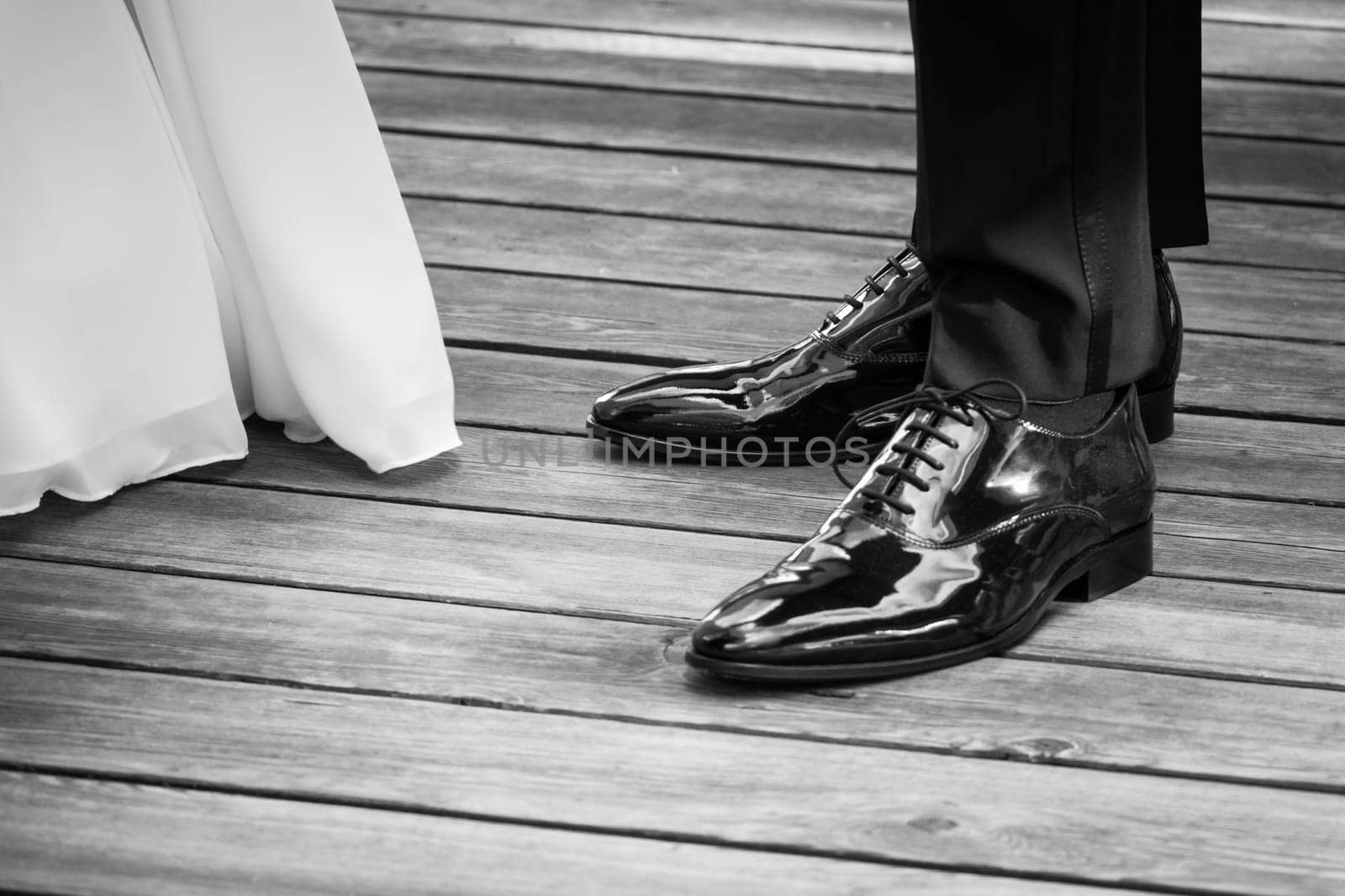 The man and the woman wearing luxury lifestyle bridal dress, suit and shoes. The Male shoe luster is polished. Wooden floor copyspace.