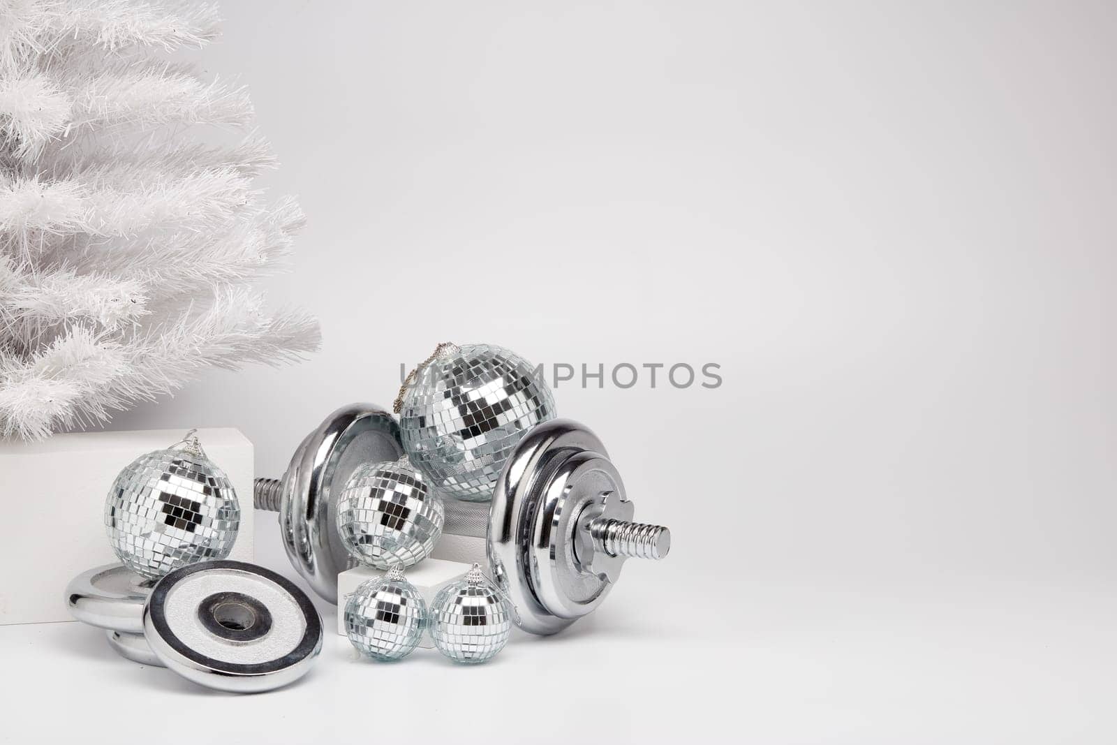 Dumbbells, Christmas fir tree and mirorr balls on white background with copy space. For design of advertising, web design. Christmas and New Year. Fitness, sport or healthy lifestyle concept.