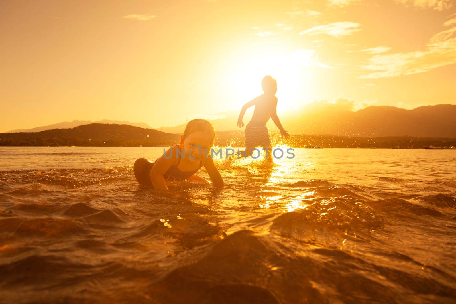 cheerful children play in the sea at sunset, running child and little girl in the foreground.