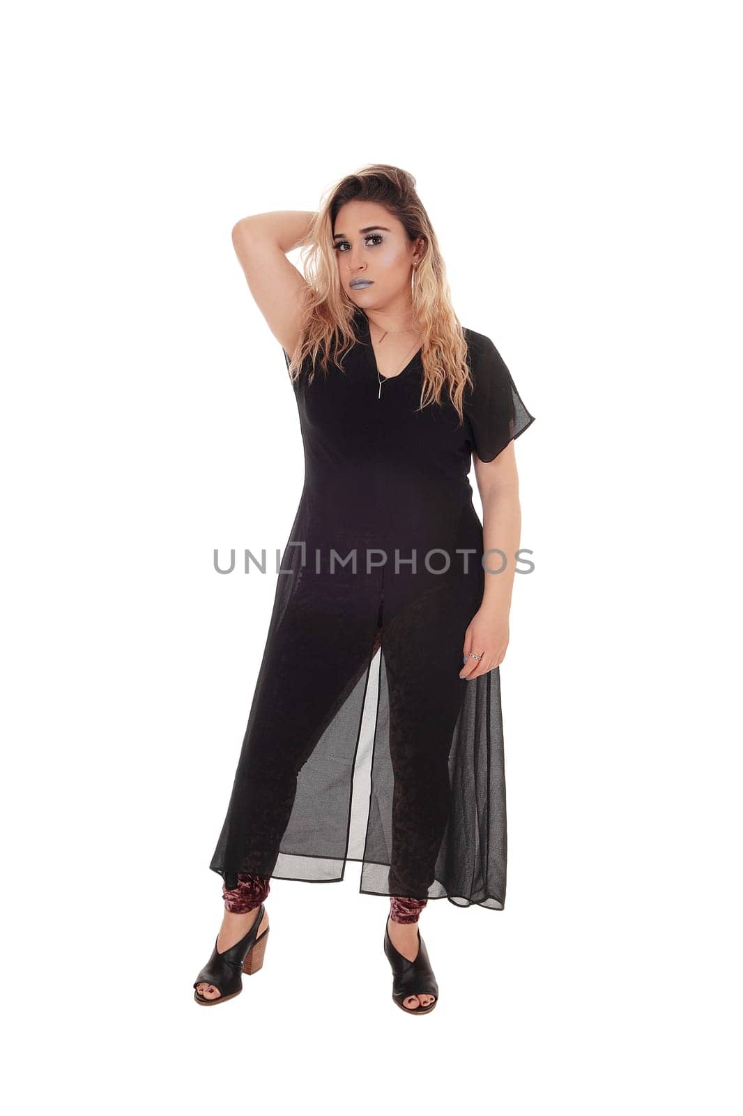 A lovely young woman standing front the front in black tights and a.black dress with one hand behind head, isolated for white background.