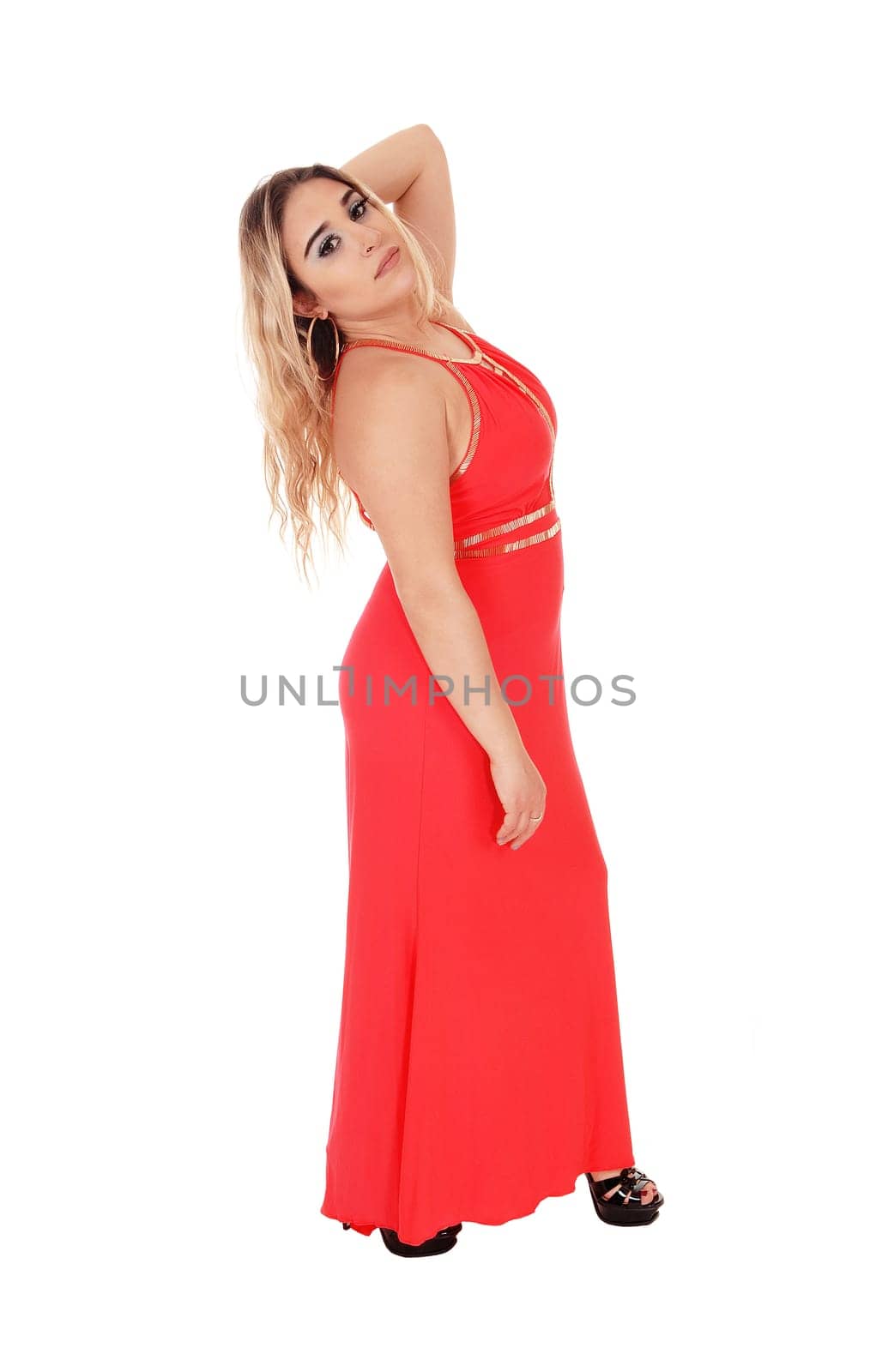 Lovely young woman standing in a long red evening dress in profile.with one hand behind her head, isolated for white background.