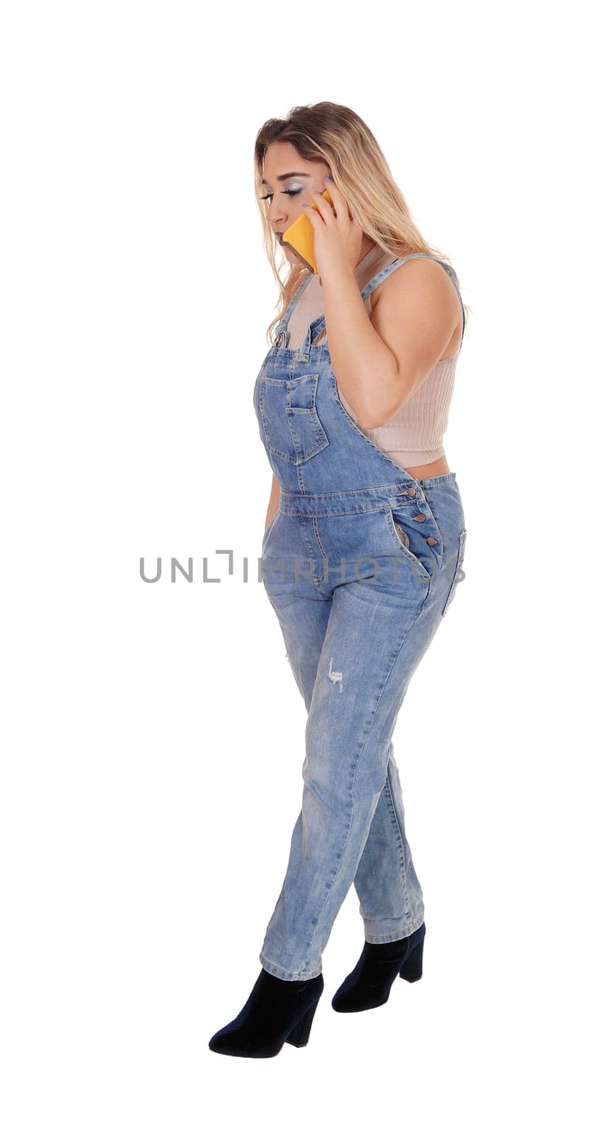 A gorgeous young woman standing in profile in working jeans and.talking on her cell phone, isolated for white background.