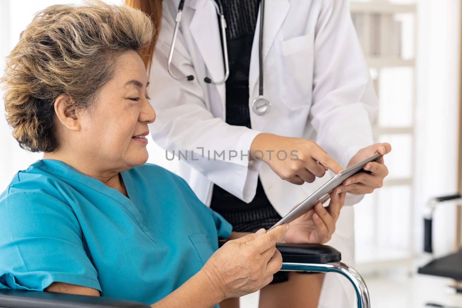 Asian confidence doctor using digital tablet expressing health concerns with old elderly woman patient sit on wheelchair