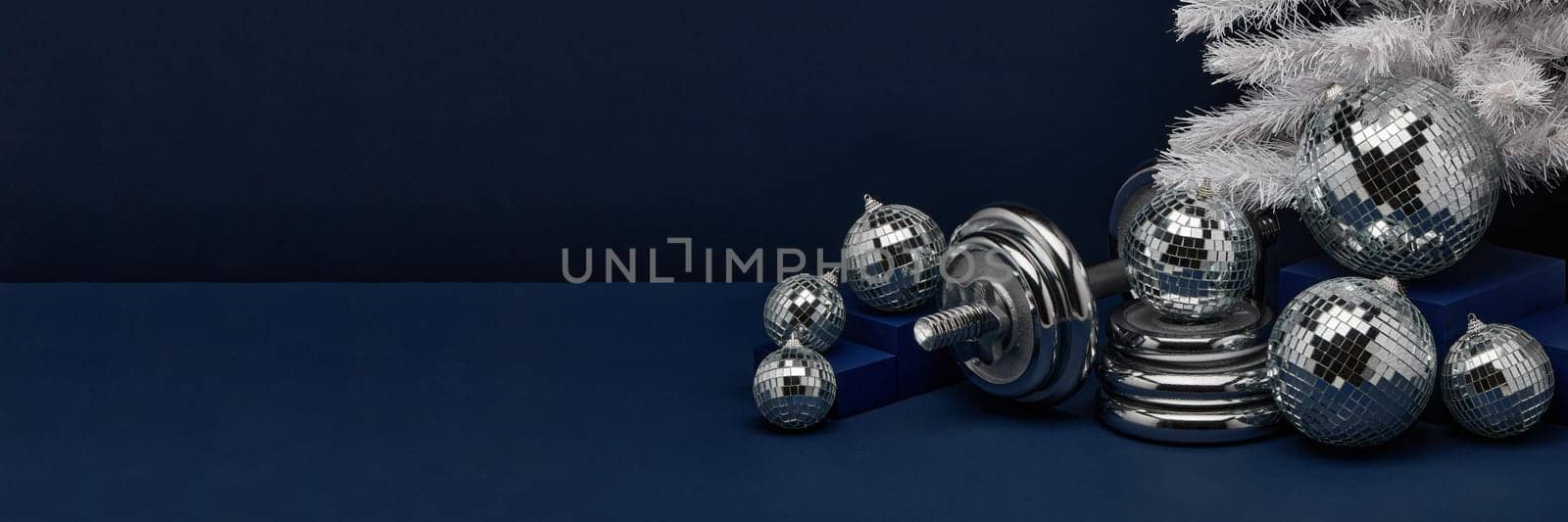 Dumbbells, Christmas fir tree and mirorr balls on dark blue background with copy space. For design of advertising, web design. Christmas and New Year. Fitness, sport or healthy lifestyle concept.