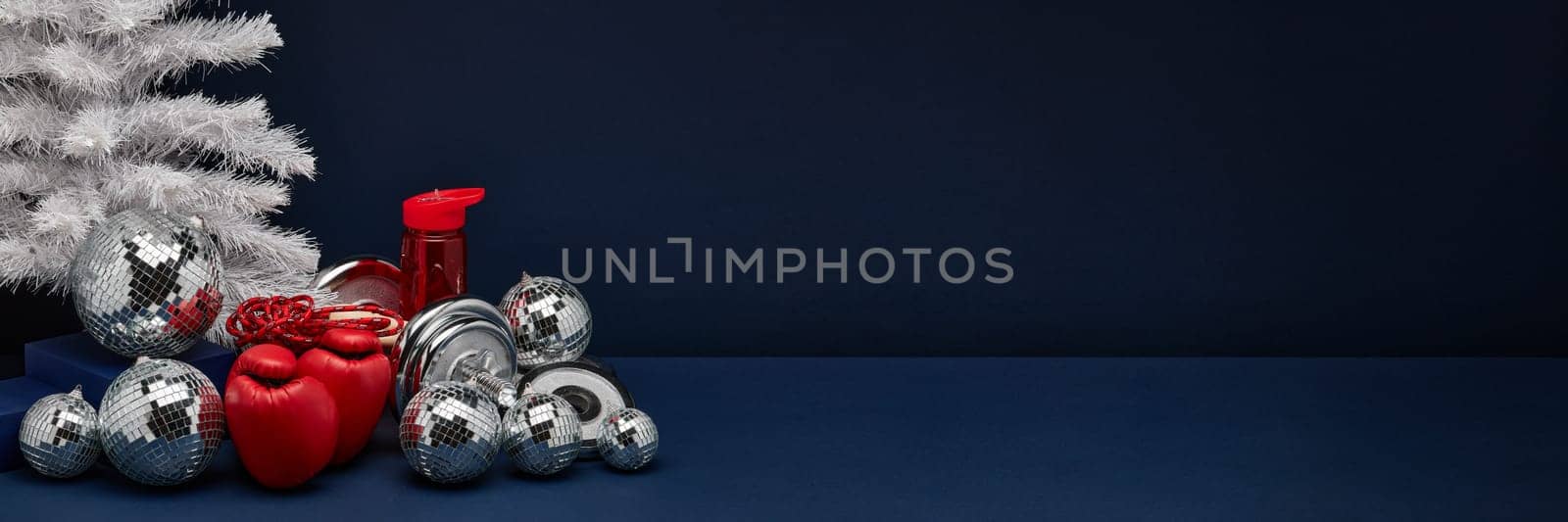 Dumbbell, boxing gloves, skipping rope, Christmas decoration on dark blue background with copy space. For design of advertising, web design. Christmas and New Year. Fitness, sport or healthy lifestyle