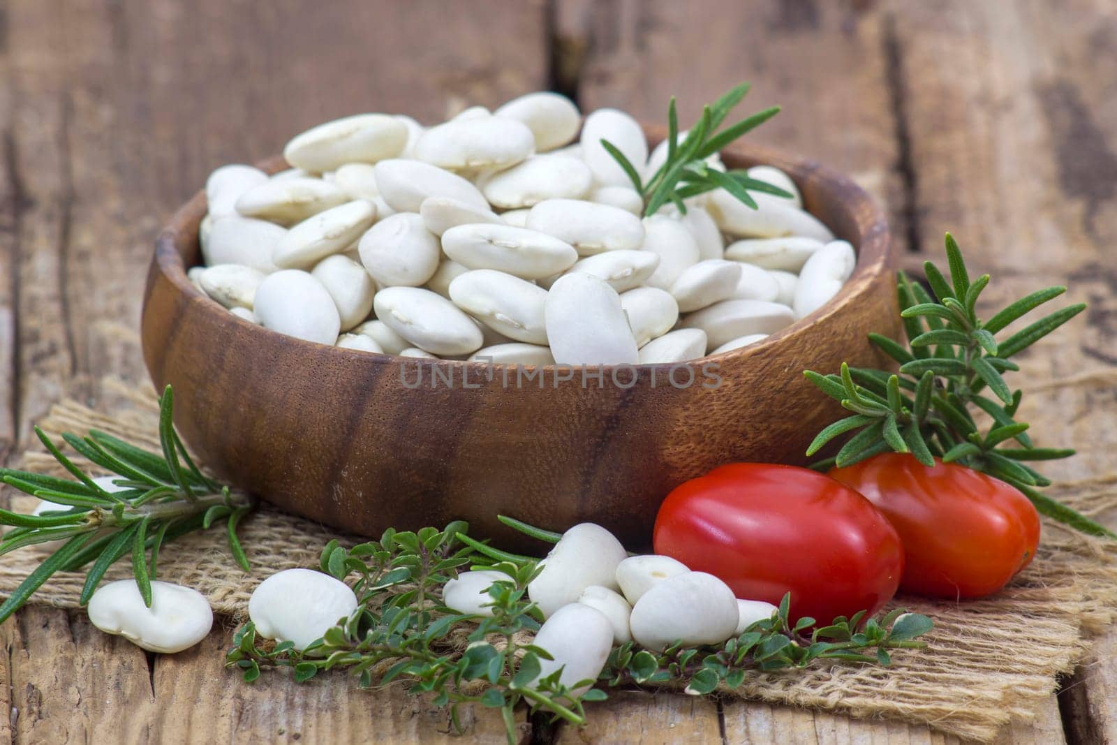 white beans, tomatoes and herbs on wooden background