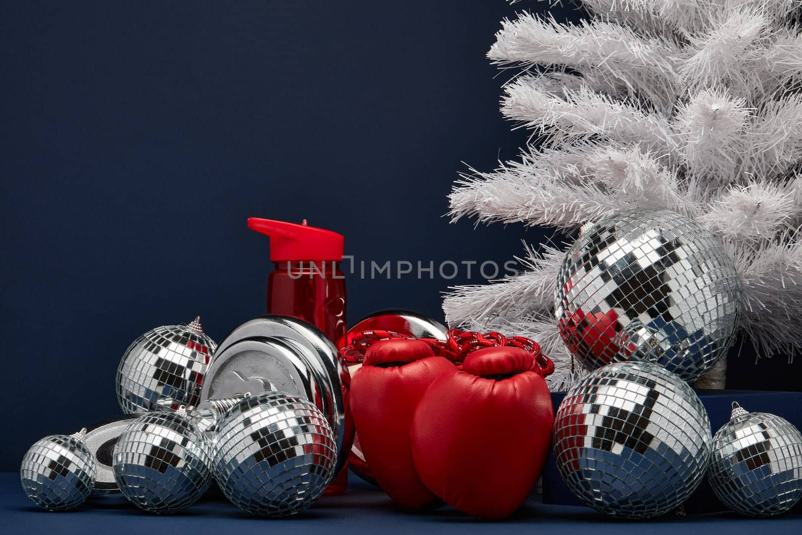 Dumbbell, boxing gloves, skipping rope, Christmas decoration on dark blue background with copy space. For design of advertising, web design. Christmas and New Year. Fitness, sport or healthy lifestyle