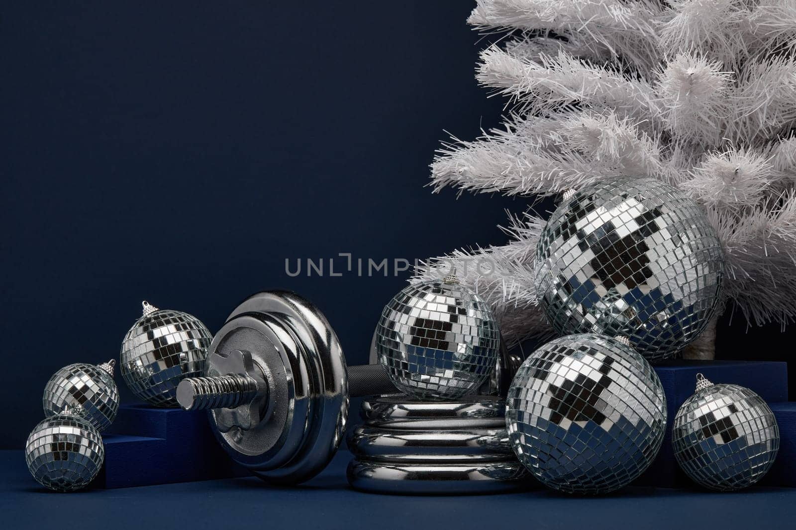 Dumbbells, Christmas fir tree and mirorr balls on dark blue background with copy space. For design of advertising, web design. Christmas and New Year. Fitness, sport or healthy lifestyle concept.