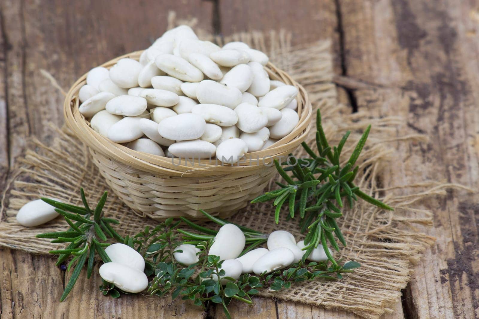 white beans and herbs in a basket on wooden background