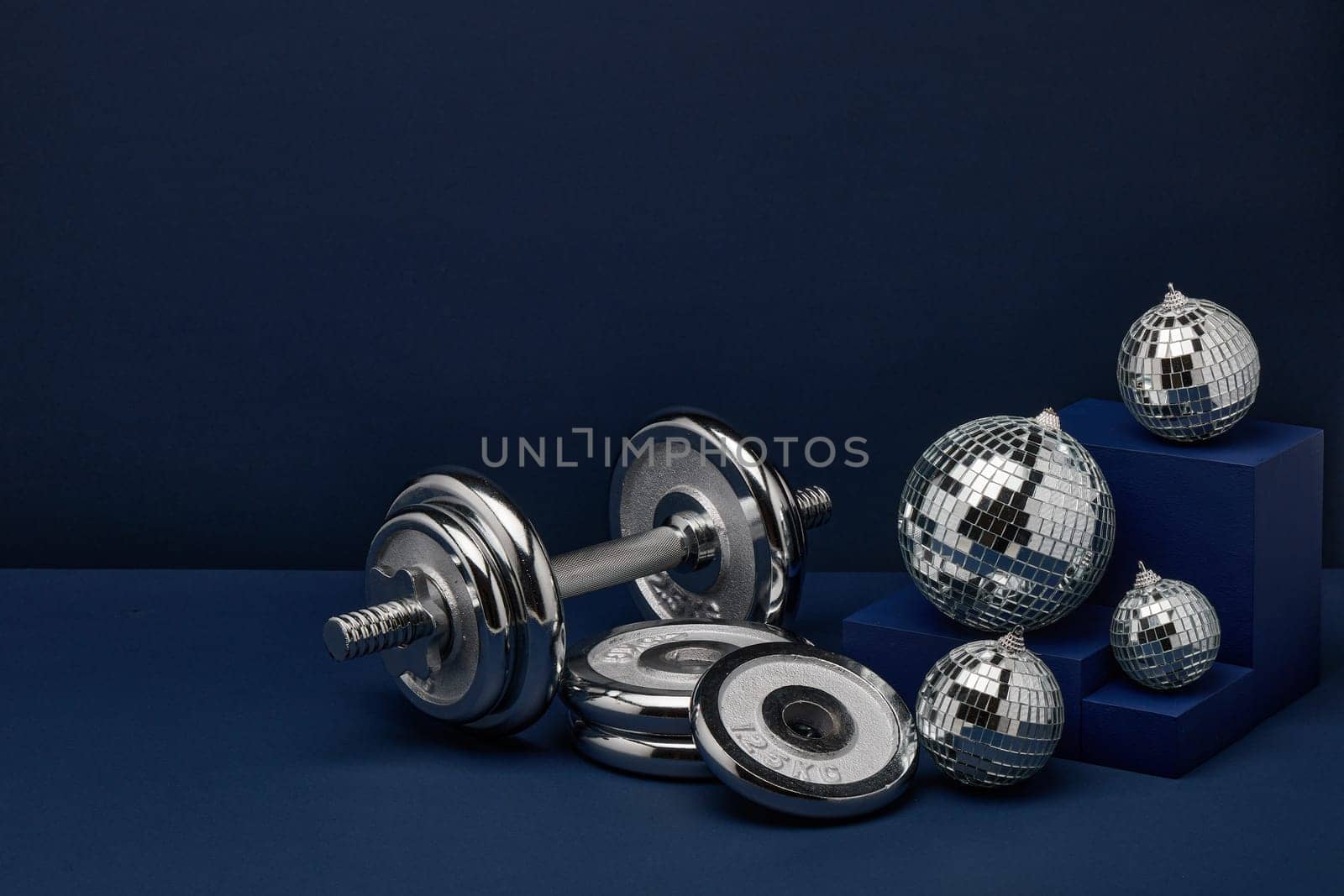 Dumbbell with weights and mirorr balls on dark blue background with copy space. For design of advertising, web design. Christmas and New Year. Fitness, sport or healthy lifestyle concept.