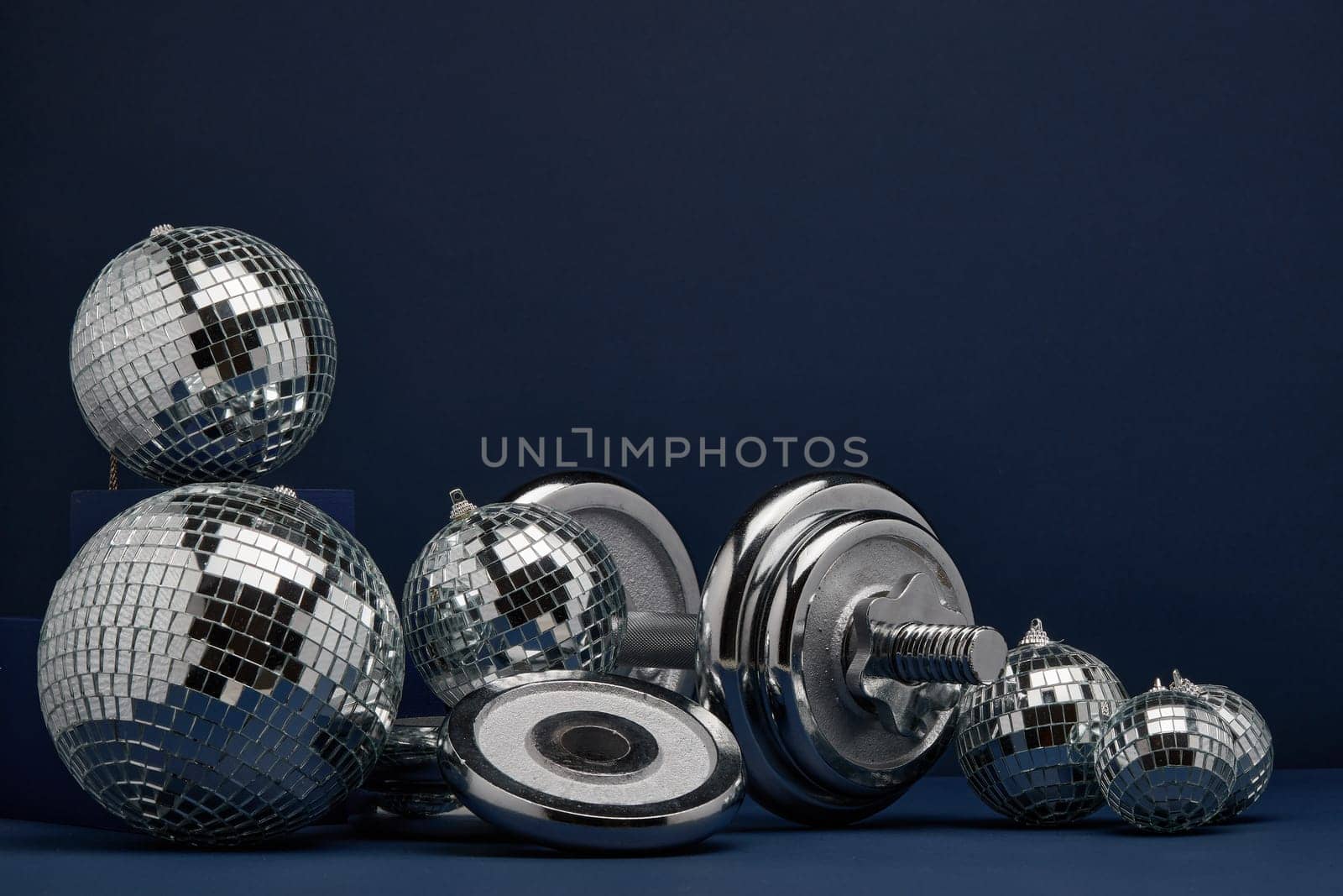 Dumbbell with weights and mirorr balls on dark blue background with copy space. For design of advertising, web design. Christmas and New Year. Fitness, sport or healthy lifestyle concept.