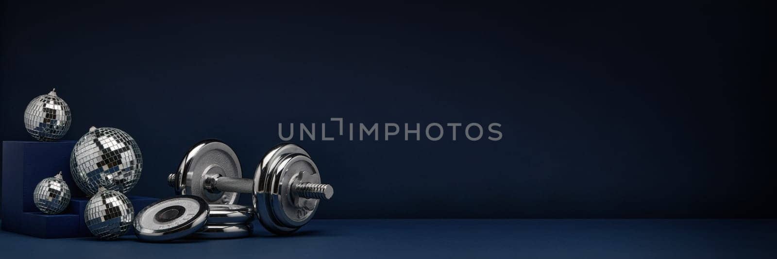 Dumbbell with weights and mirorr balls on dark blue background with copy space. For design of advertising, web design. Christmas and New Year. Fitness, sport or healthy lifestyle concept.