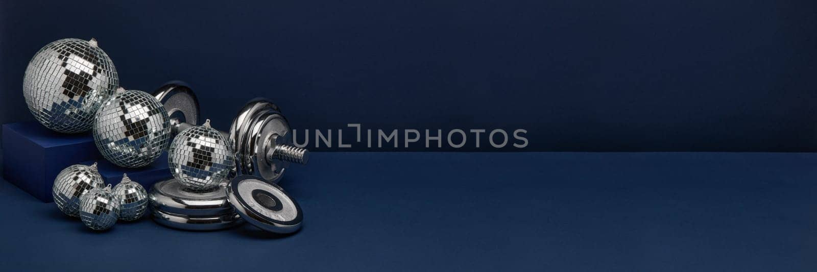 Dumbbell with weights and mirorr balls on dark blue background with copy space. For design of advertising, web design. Christmas and New Year. Fitness, sport or healthy lifestyle concept.