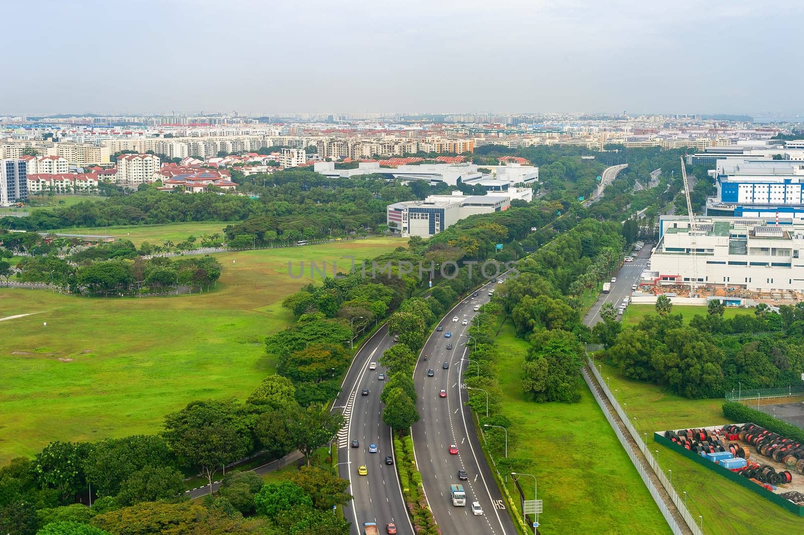 Aerial view of Singapore with car traffic on highway, green landscape with modern citysape in background