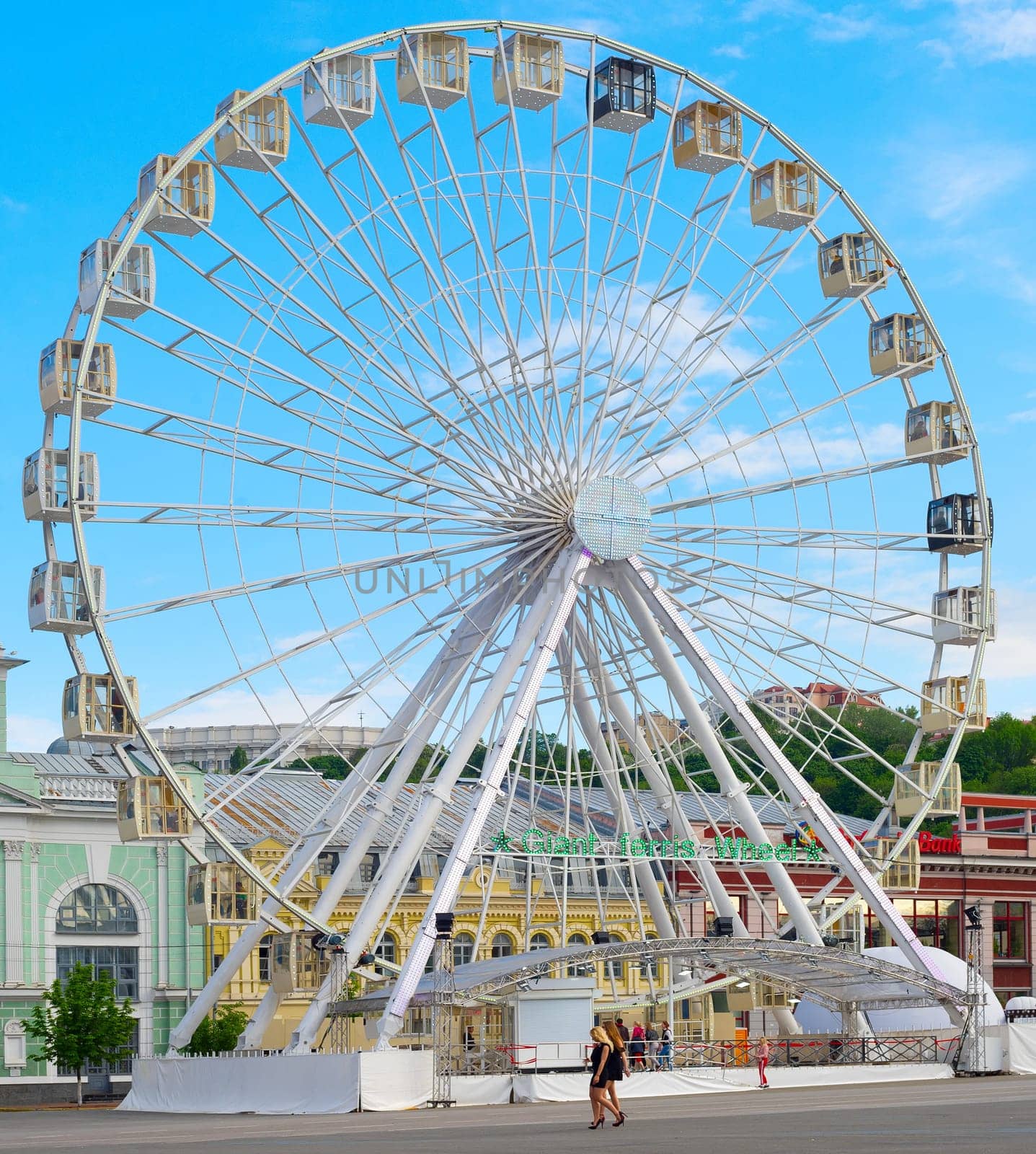 KIEV, UKRAINE - MAY 11, 2019: People walking by giant Ferries Wheel in Kiev, Ukraine. St. Andrew chuch in the background