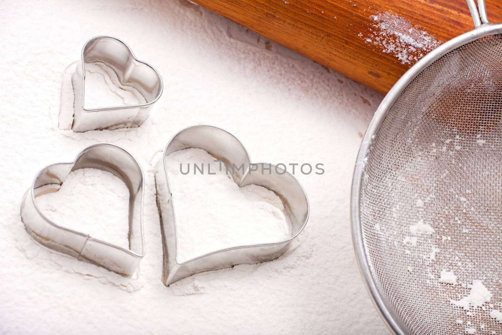 Cookie cutters, flour sieve and wooden rolling pin on a floured baking mat