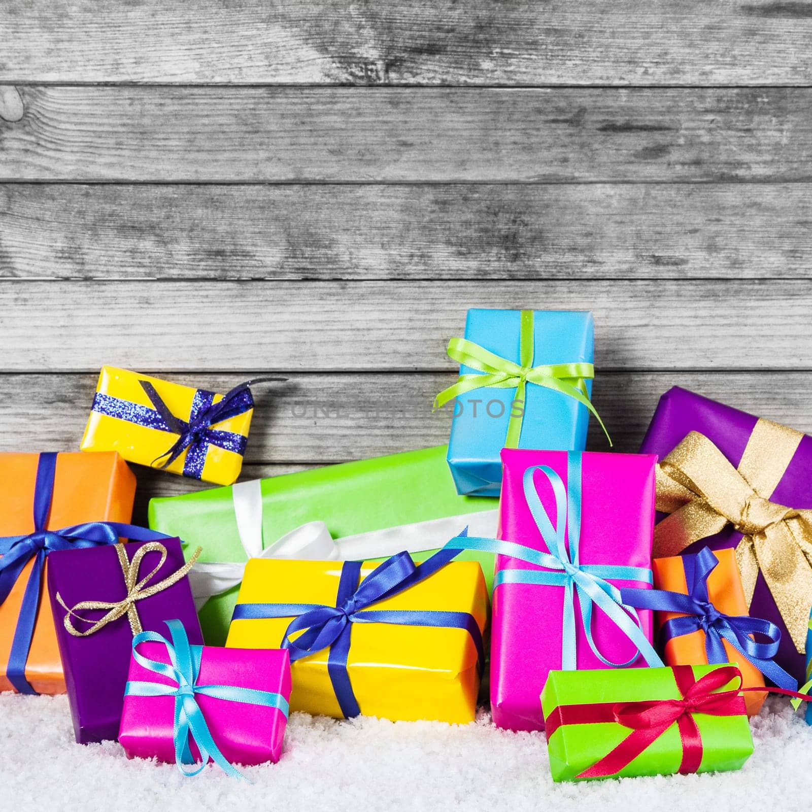 Close up Assorted Colored Christmas Gift Boxes with Ribbons on Snow with Wooden Wall Background.