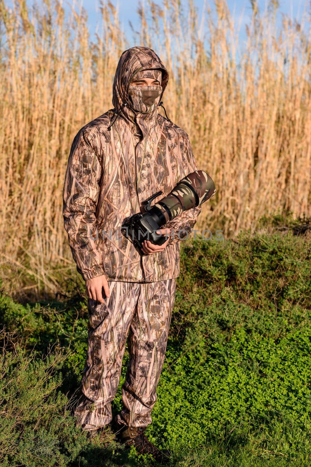 Naturalist photographer in action, with camouflage and camera, in the wilderness.