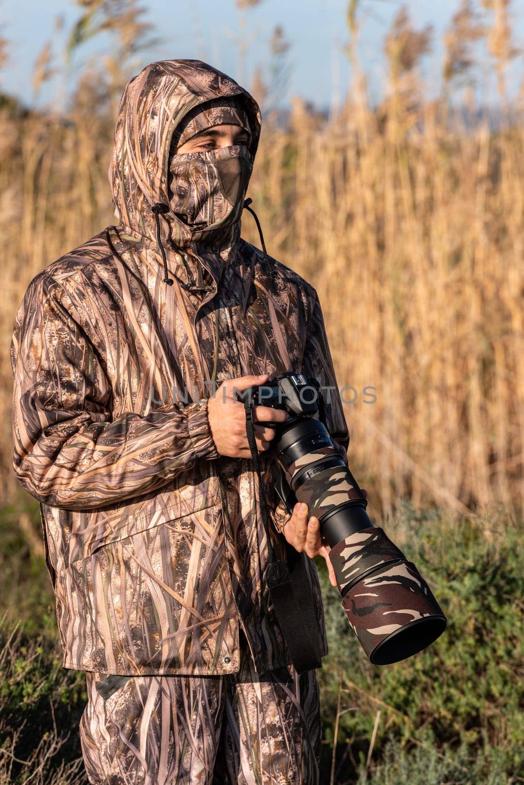 Naturalist photographer in action, with camouflage and camera, in the wilderness.