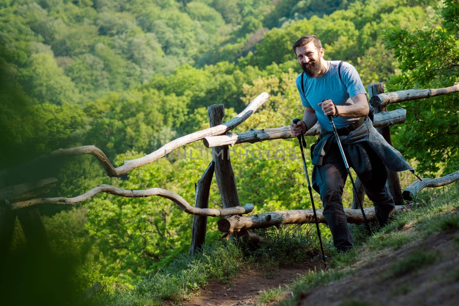 The smiling bearded man is walking with hiking sticks in nature on natural green backgound, active life and adventure concept.