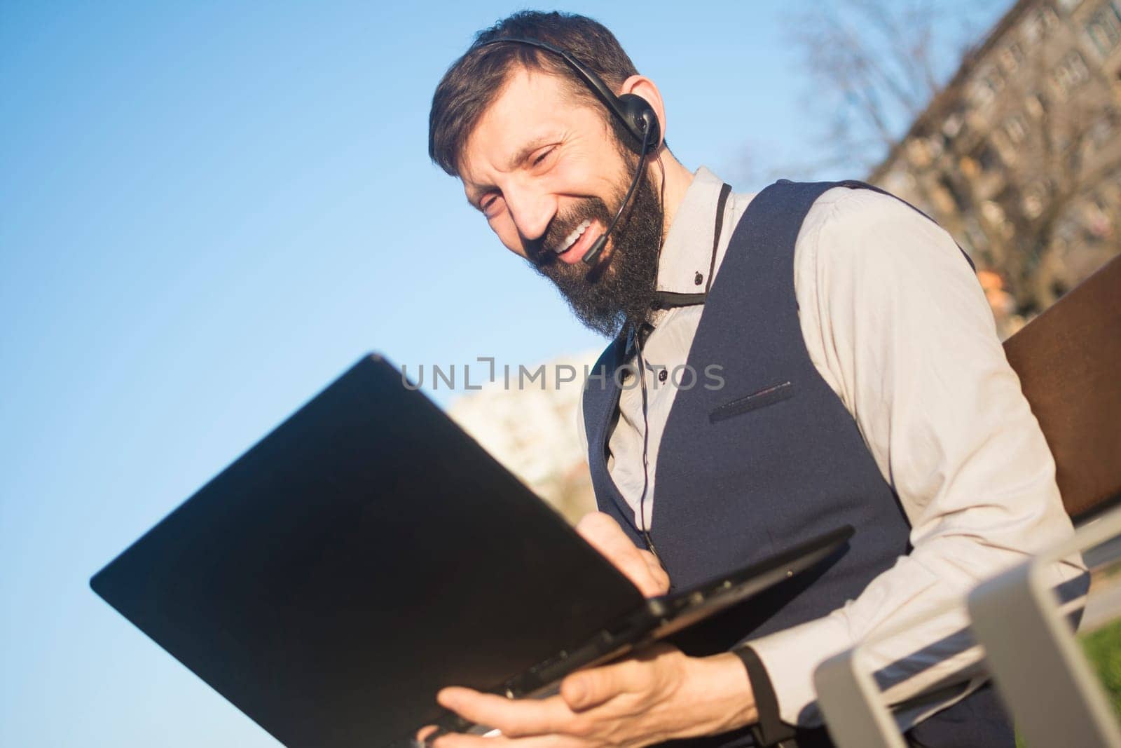 The consultant is consulting with client online and working on his laptop outdoors, freelancing concept.