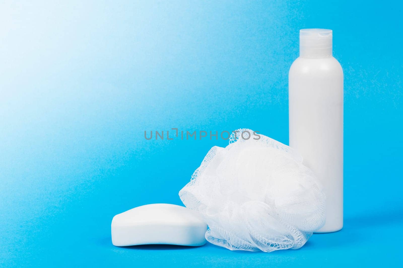 White shower set with soap, bath sponge and shower gel is on blue background.