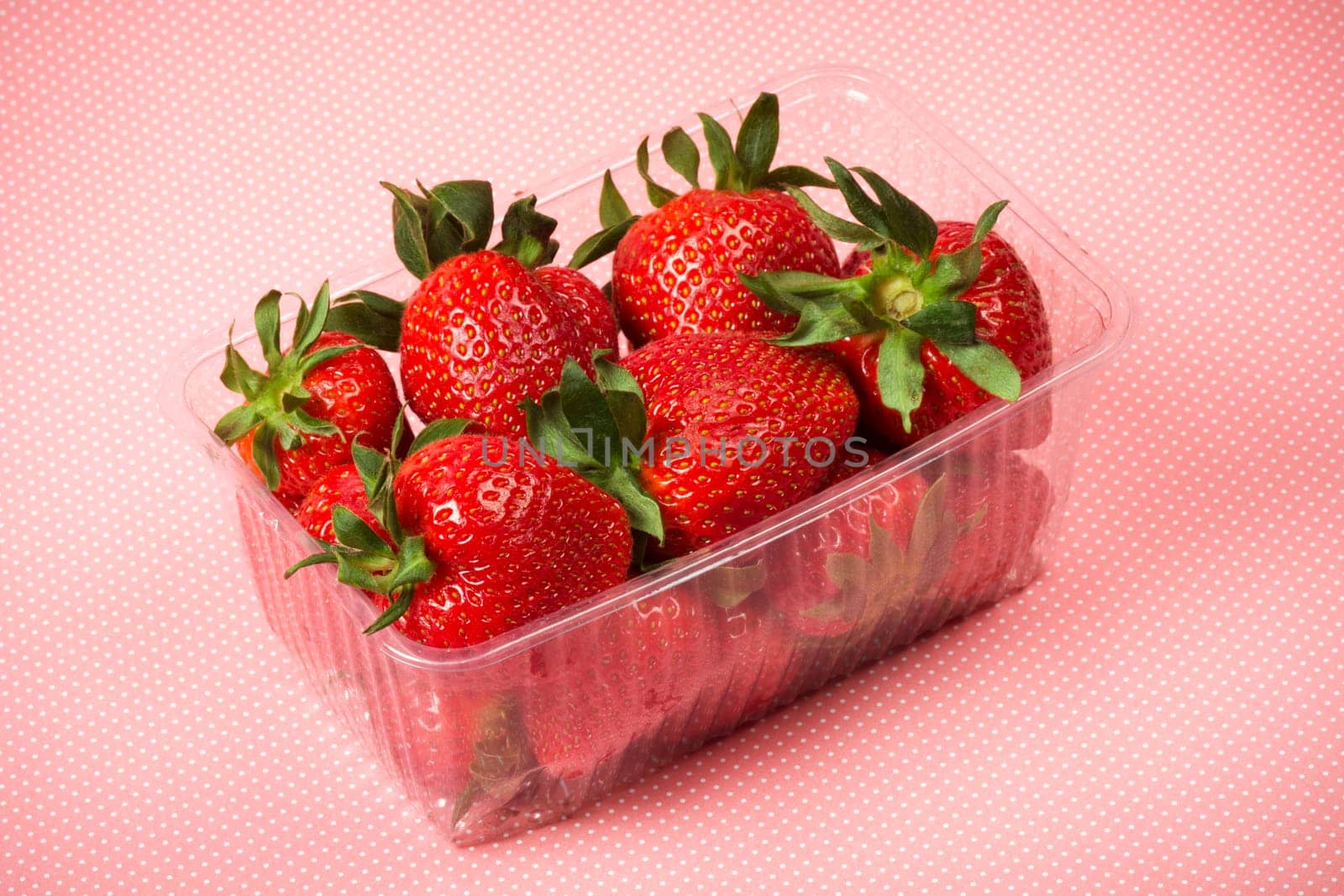 Red ripe strawberries in plastic package on pink spotted background.