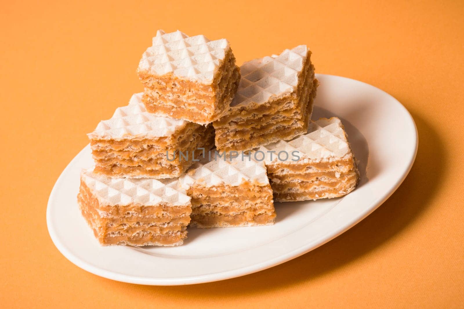Filled wafer cake dessert on white plate on orange background.