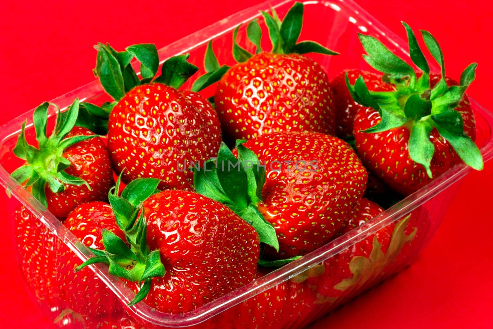 Red ripe strawberries are in plastic package on red background.