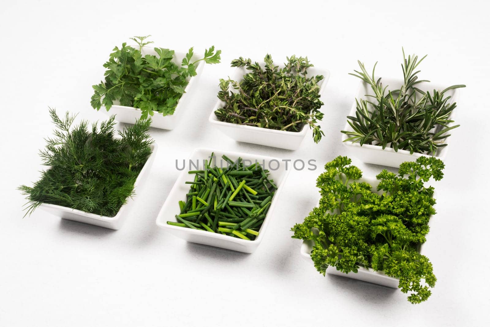 Fresh green herbs and spices are in white dish on white background.