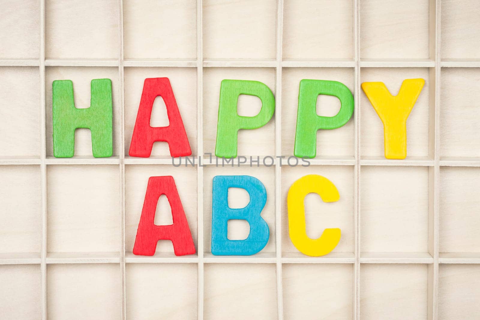 The HAPPY ABC text from colorful wooden letters is on wooden background, learning alphabet.